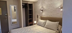 Une chambre à coucher comprenant un lit, une armoire, un miroir et un mur avec un motif en briques.