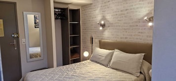 Un dormitorio con cama, armario, espejo y pared con diseño de ladrillo.