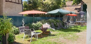 A backyard with outdoor furniture, including chairs and a table, under two umbrellas. - Le Faubourg (Figeac)