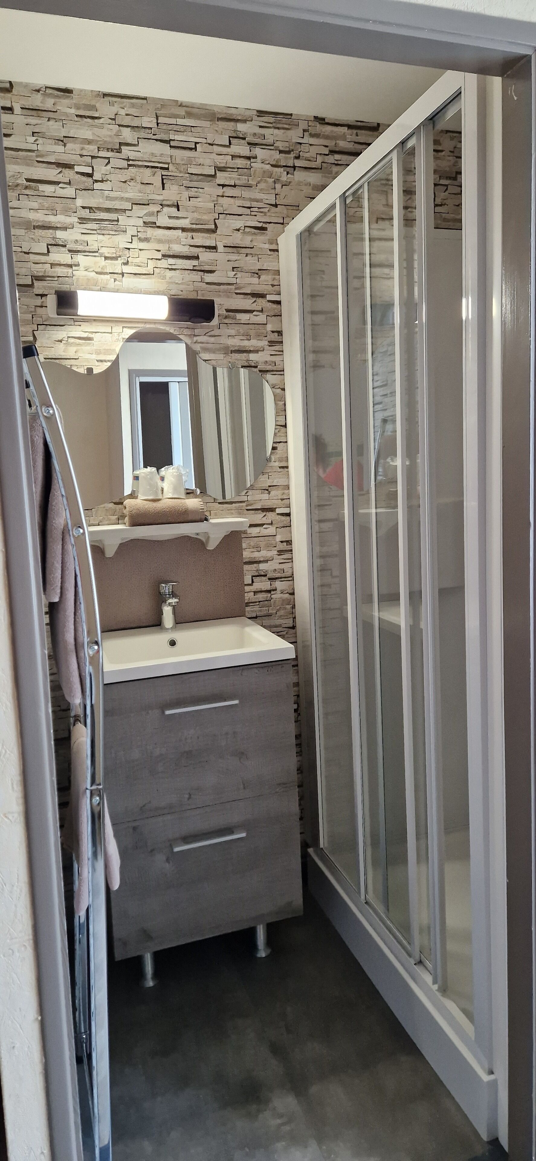 Une salle de bain avec un mur en pierre derrière le lavabo, un lavabo avec un miroir et une douche dotée de portes en verre dépoli.