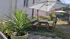 A patio with a wooden table and benches, an umbrella, and potted plants. - Le Faubourg (Figeac)
