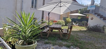 Un patio con mesa y bancos de madera, una sombrilla y plantas en macetas.