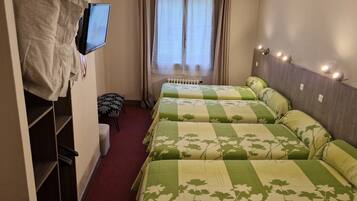 A hotel room with three beds, a TV mounted on the wall, a small table, and a window with curtains.
