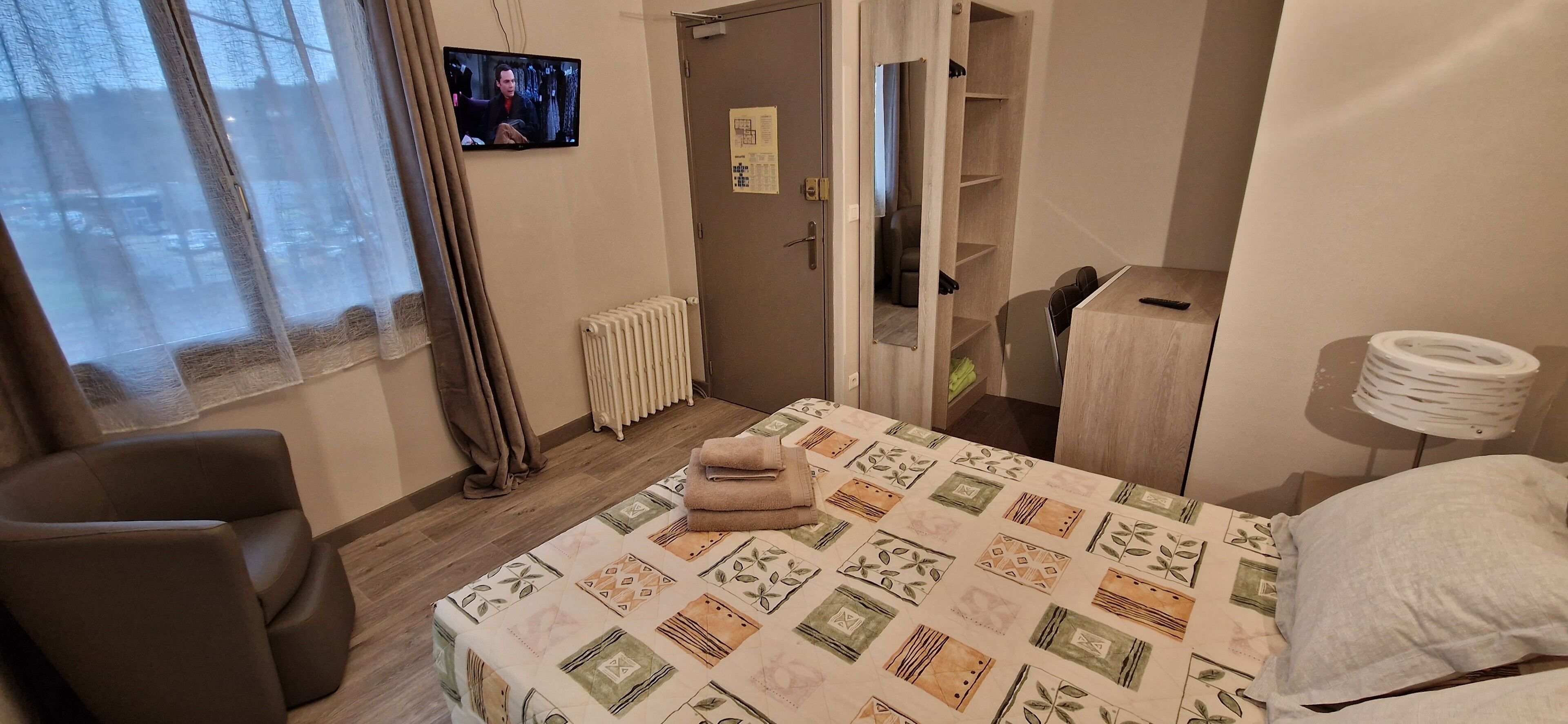 Ein Schlafzimmer mit Bett, Sessel, Heizkörper, Fernseher und Kleiderschrank.