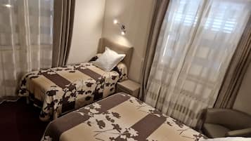 Habitación de hotel con dos camas, una mesita de noche, una silla y una ventana con cortinas.