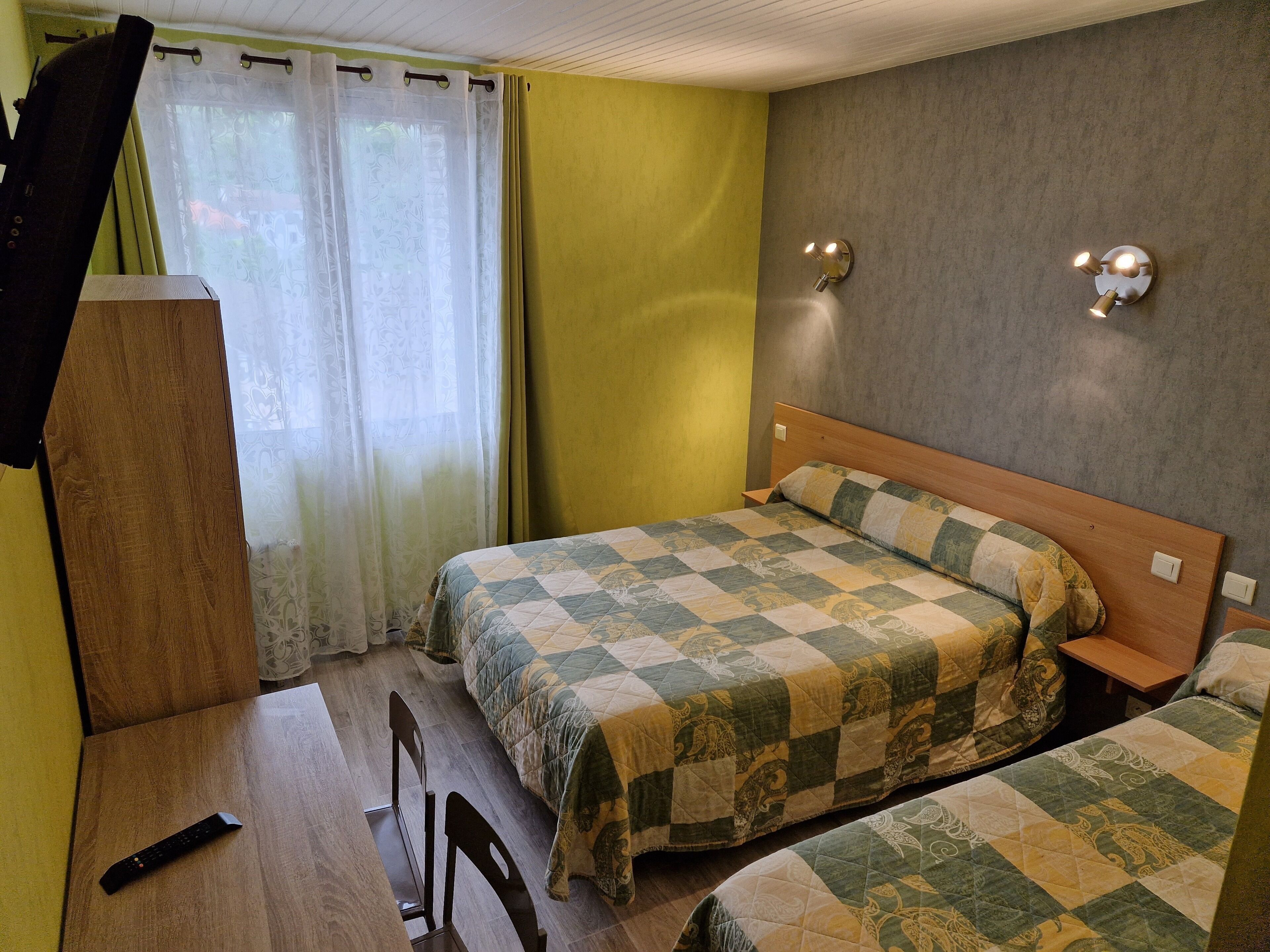 Une chambre avec deux lits, un bureau en bois, une chaise et une fenêtre avec des rideaux.