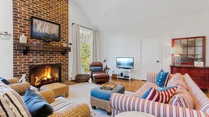 A living room with a brick fireplace, a television, and striped furniture.