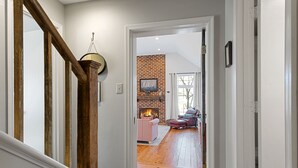 A hallway leading to a living room with a brick fireplace, striped sofa, and a pink chair.