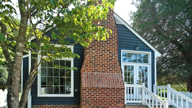 A house with a brick chimney, white railings, and a white picket fence.