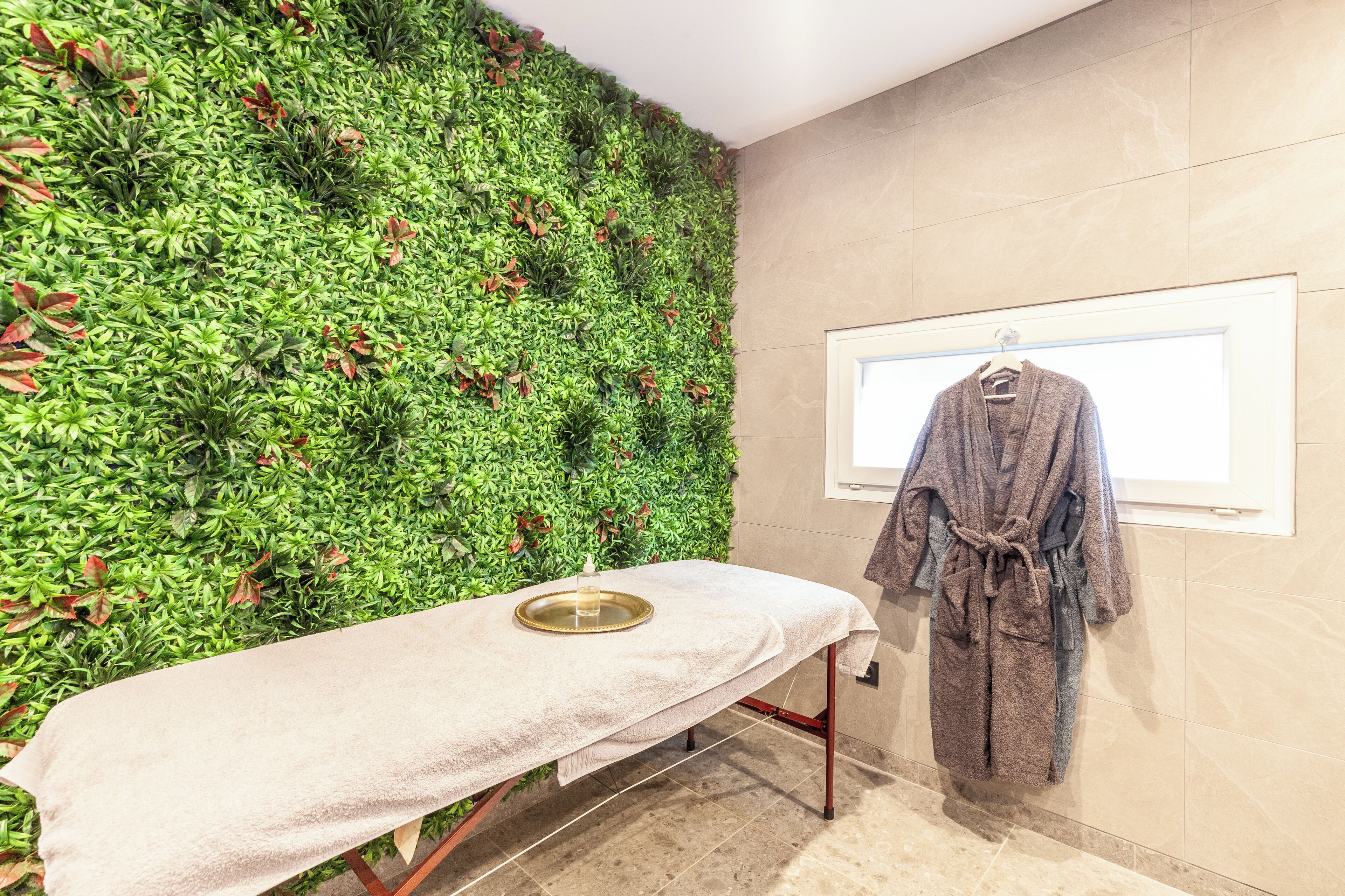 Un espace spa comprenant une table de massage, un porte-peignoir fixé au mur et un jardin vertical verdoyant.