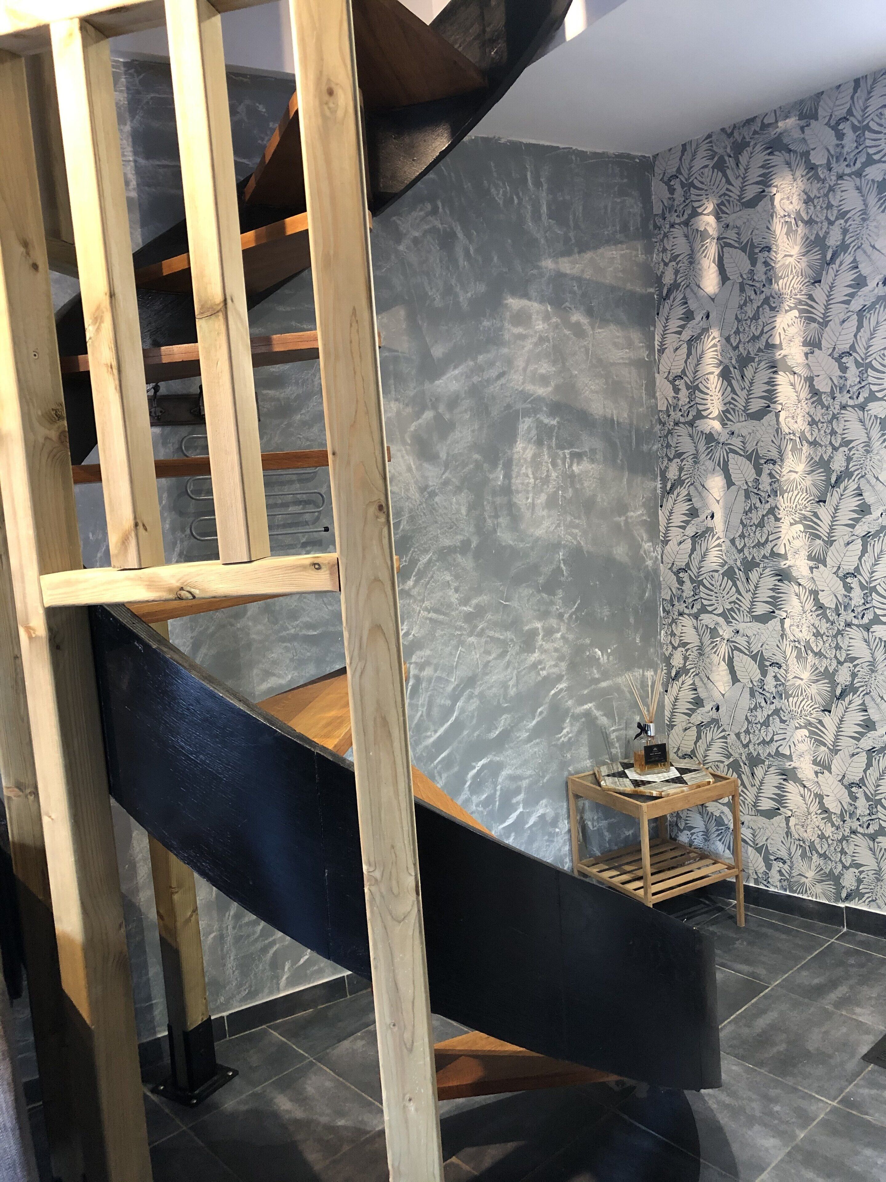 Een modern interieur met een houten trap, een zwarte metalen spiraal en bloemenbehang.