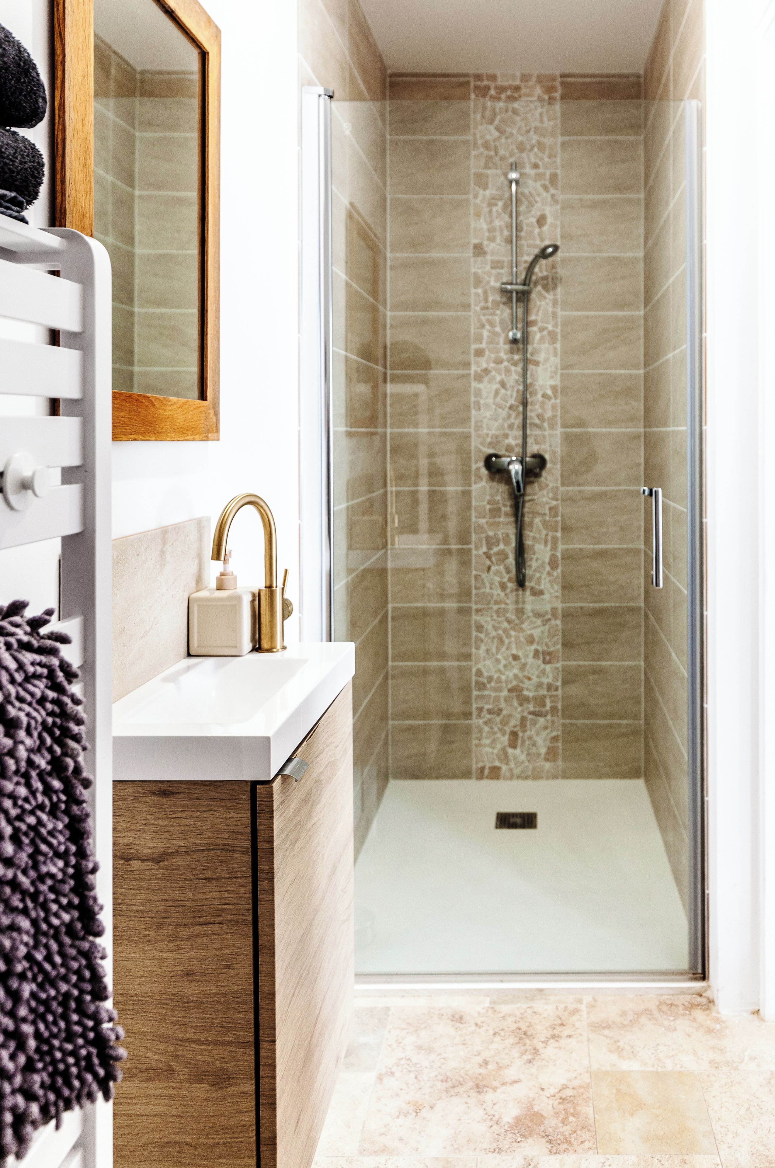 A modern bathroom with a glass-enclosed shower, a white sink with gold fixtures, and a wooden cabinet.