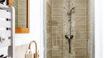 A modern bathroom with a glass-enclosed shower, a white sink with gold fixtures, and a wooden cabinet.
