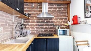 Una cocina con pared de ladrillo, extractor de acero inoxidable, microondas y cafetera roja.