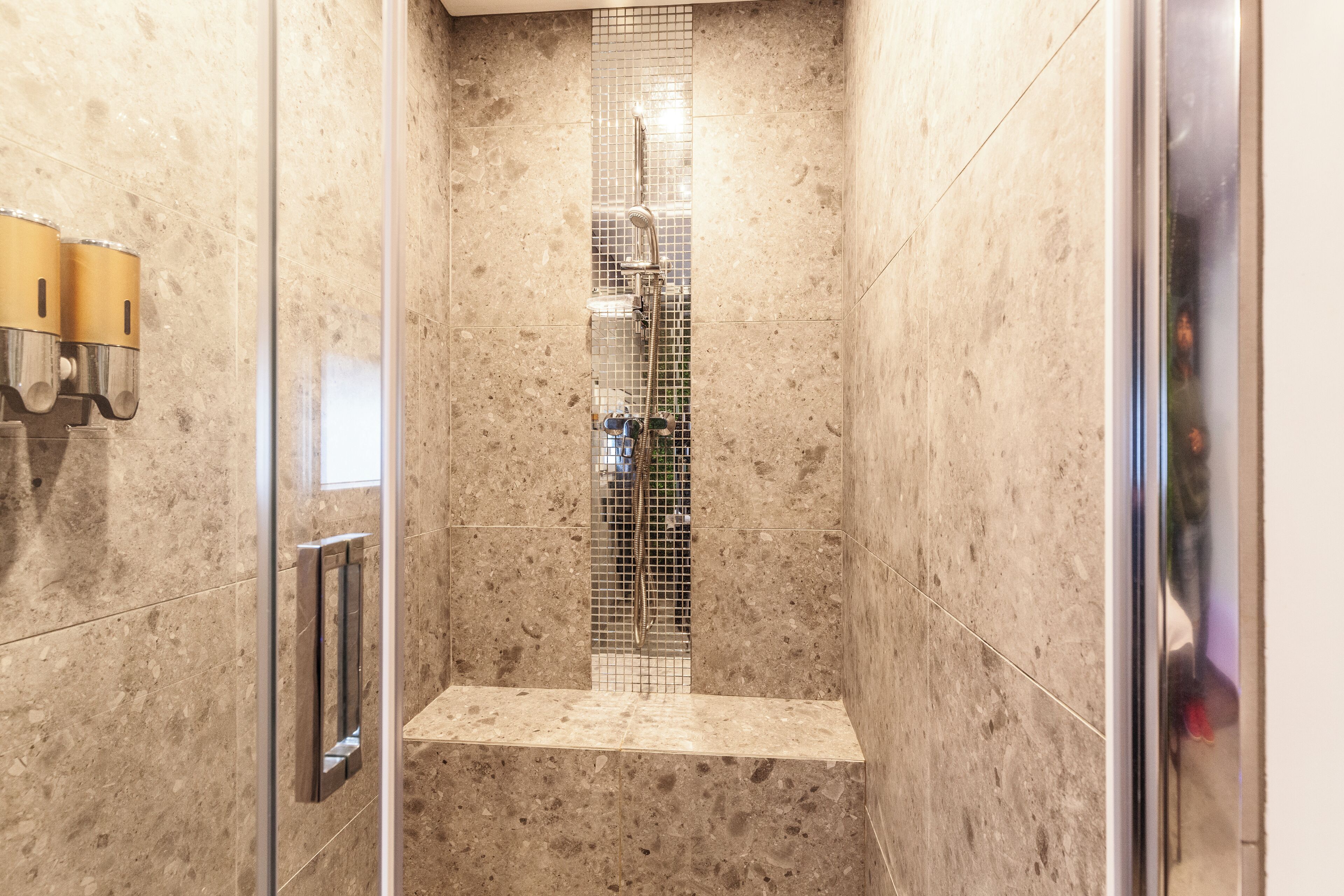 A shower with a glass door, tiled walls, and a metal showerhead.