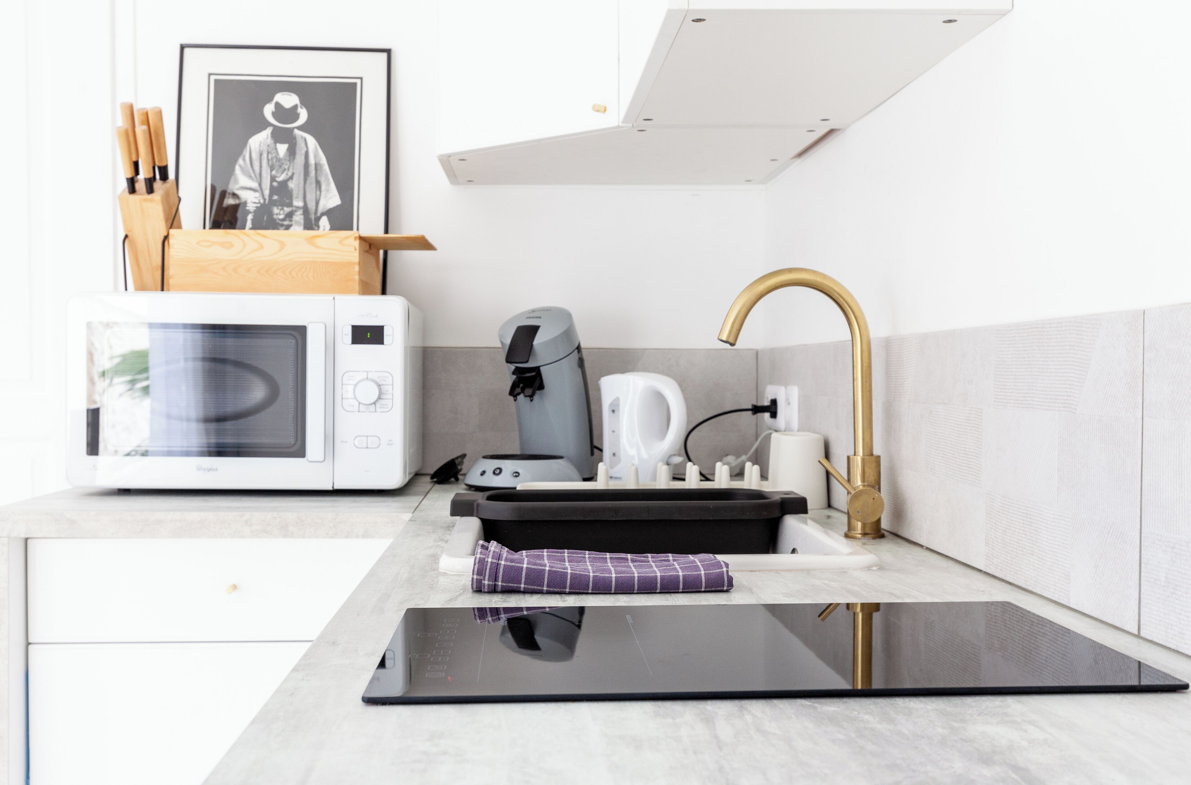 A modern kitchen with a microwave, coffee machine, and a sink with a gold faucet.