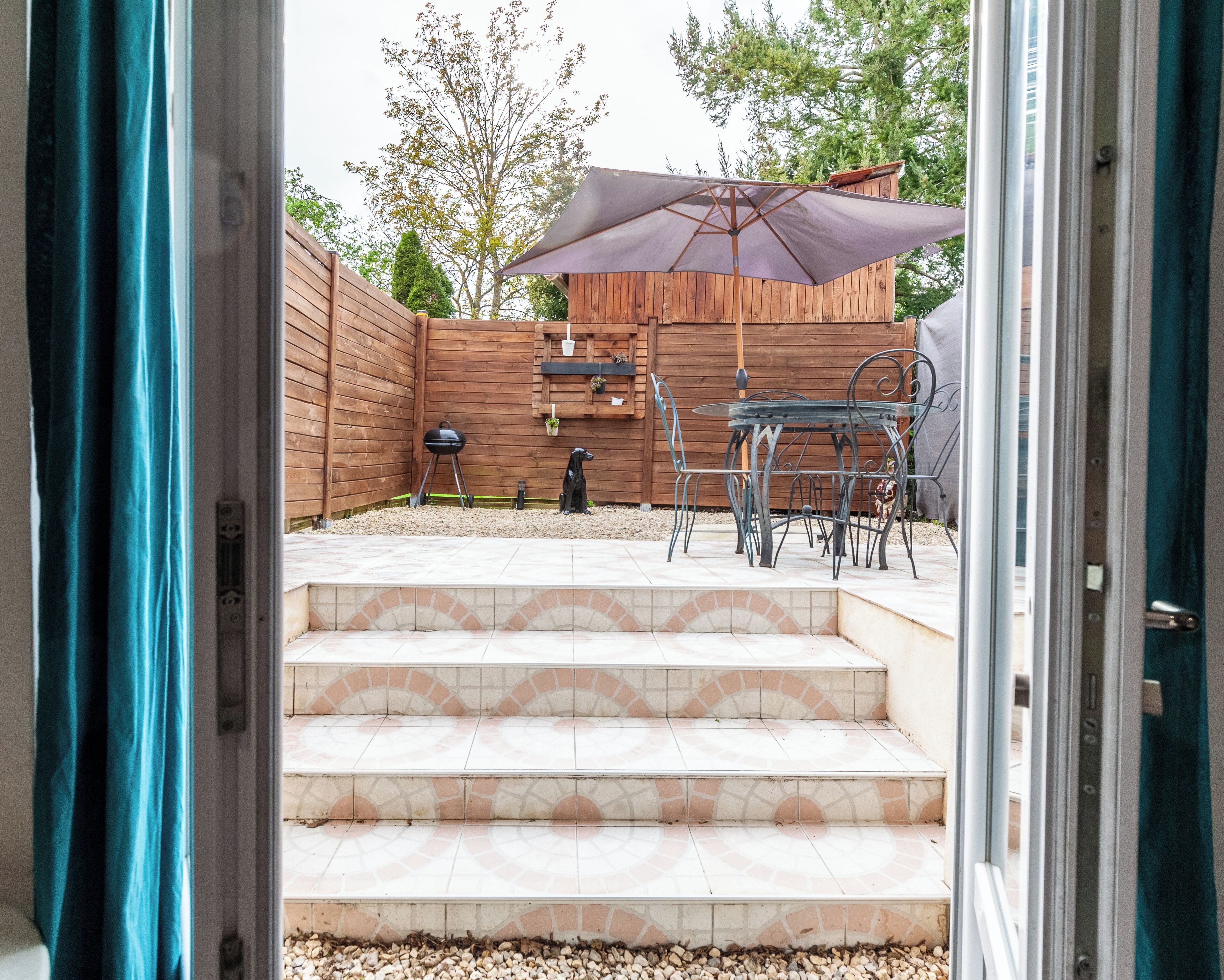 Un patio con cerca de madera, una parrilla y mobiliario exterior.