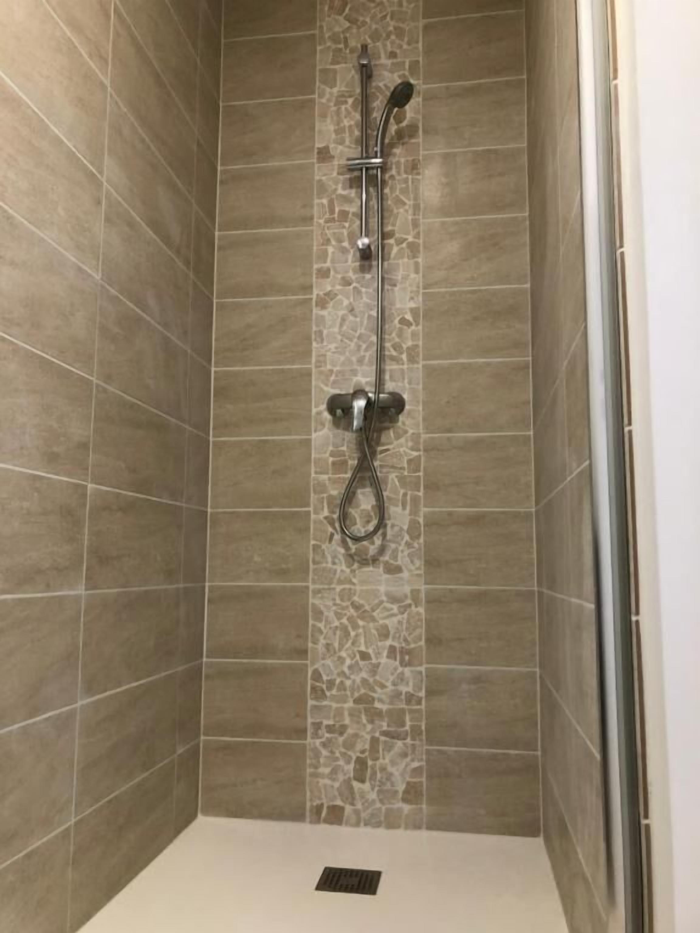 Une douche avec un mur d’accent en pierre, une douchette à main et un robinet mural.