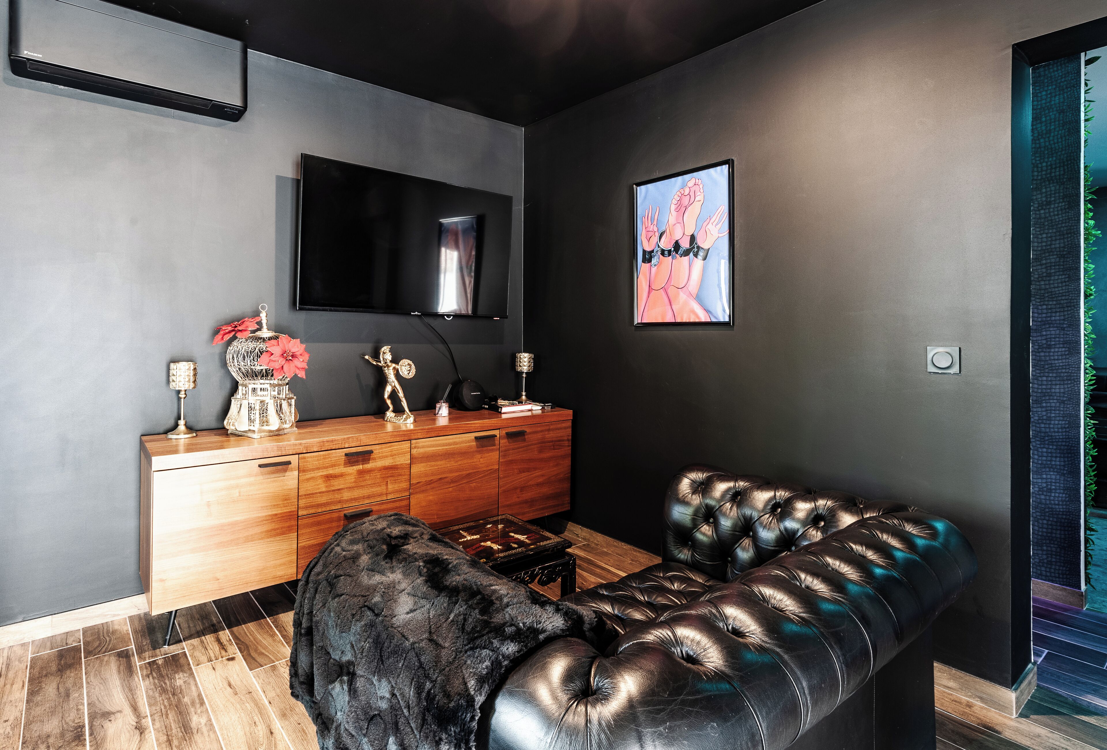 Uma sala de estar moderna com esquema de cores escuro, um sofá de couro, um armário de madeira e uma TV de tela plana fixada na parede.