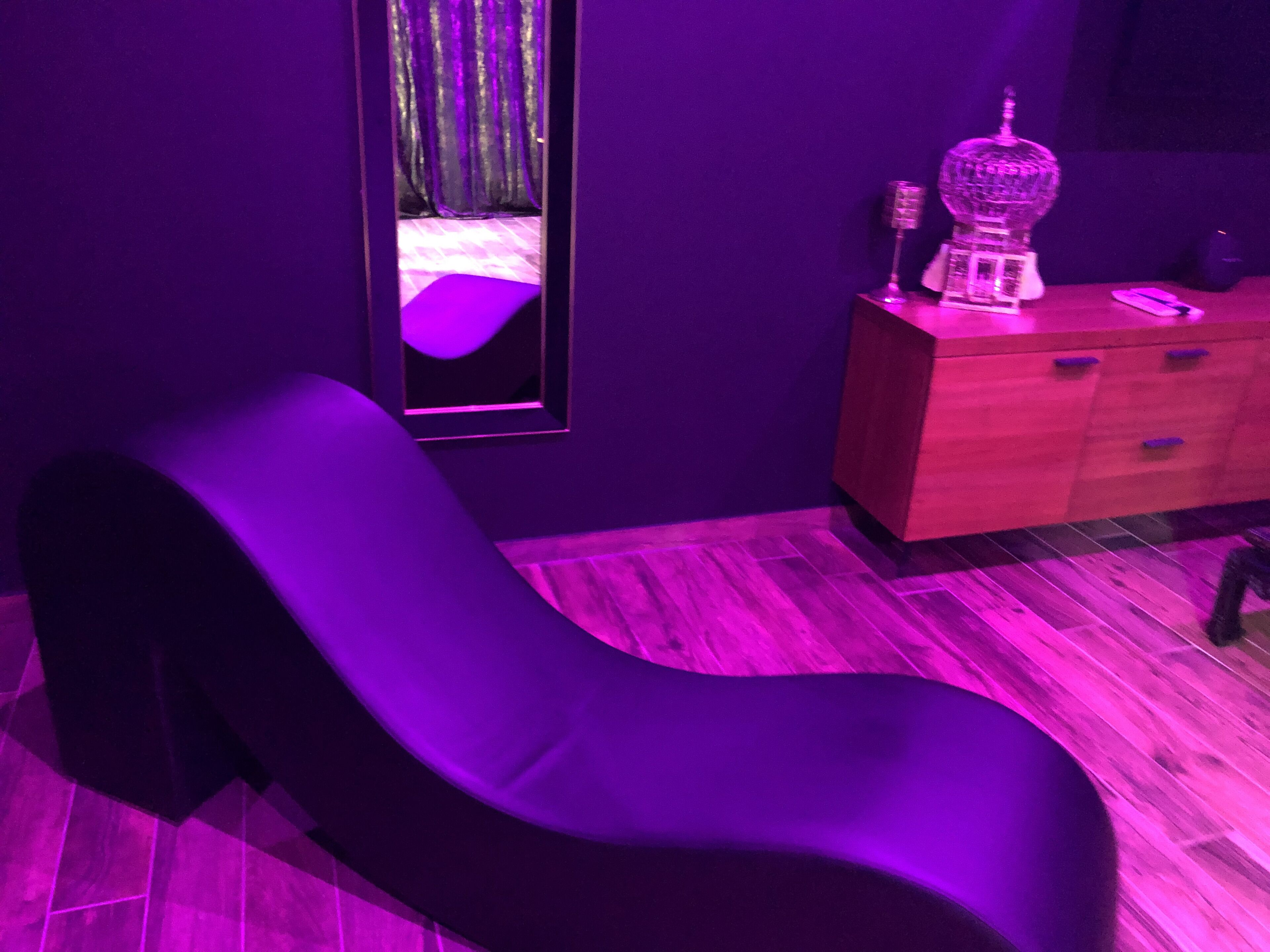 Een kamer met een donkerbruine loungestoel, een houten kast met lades en een spiegel aan de muur.