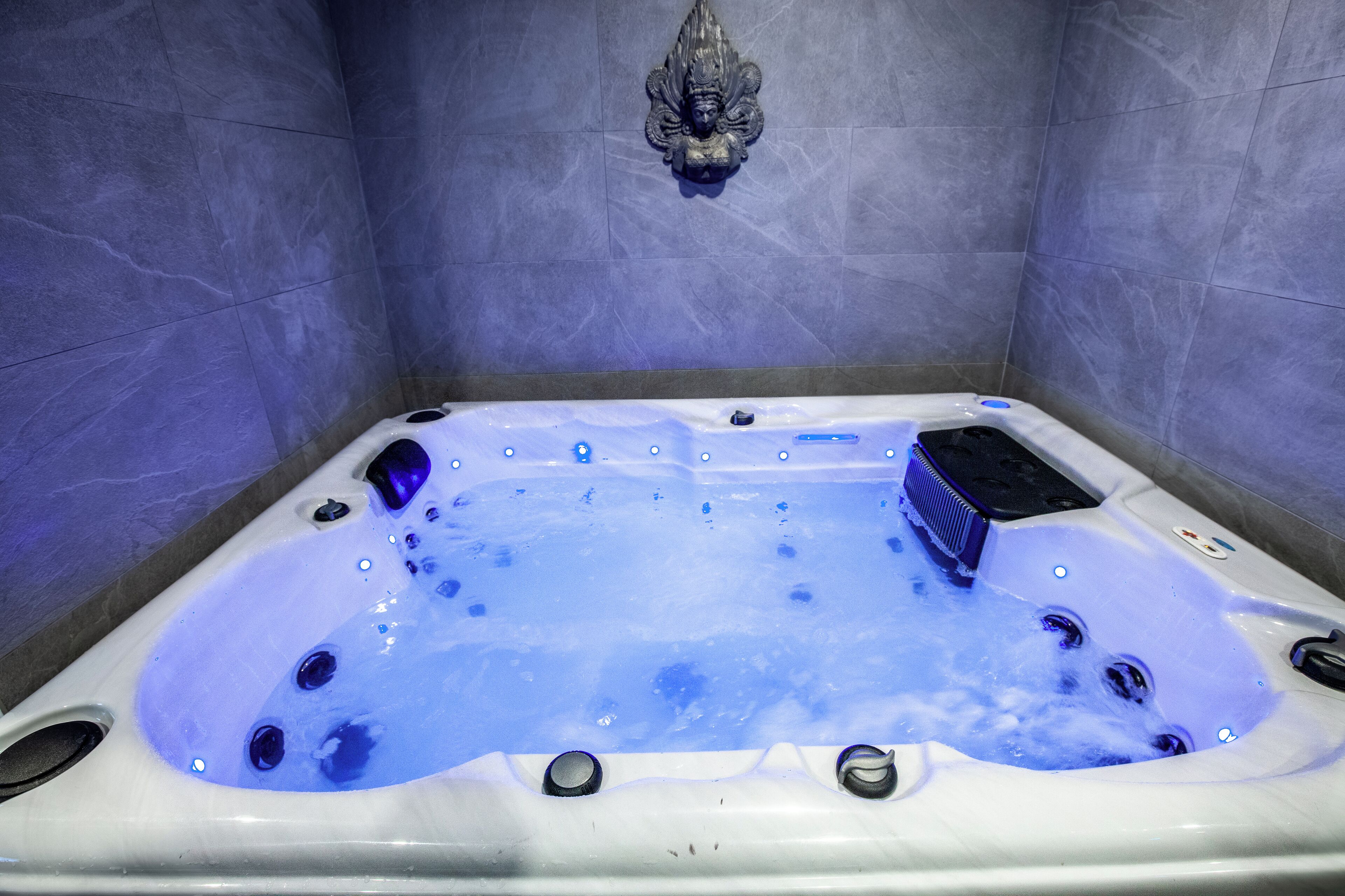 Een bubbelbad met jets, voor een betegelde muur met een decoratief element erboven.