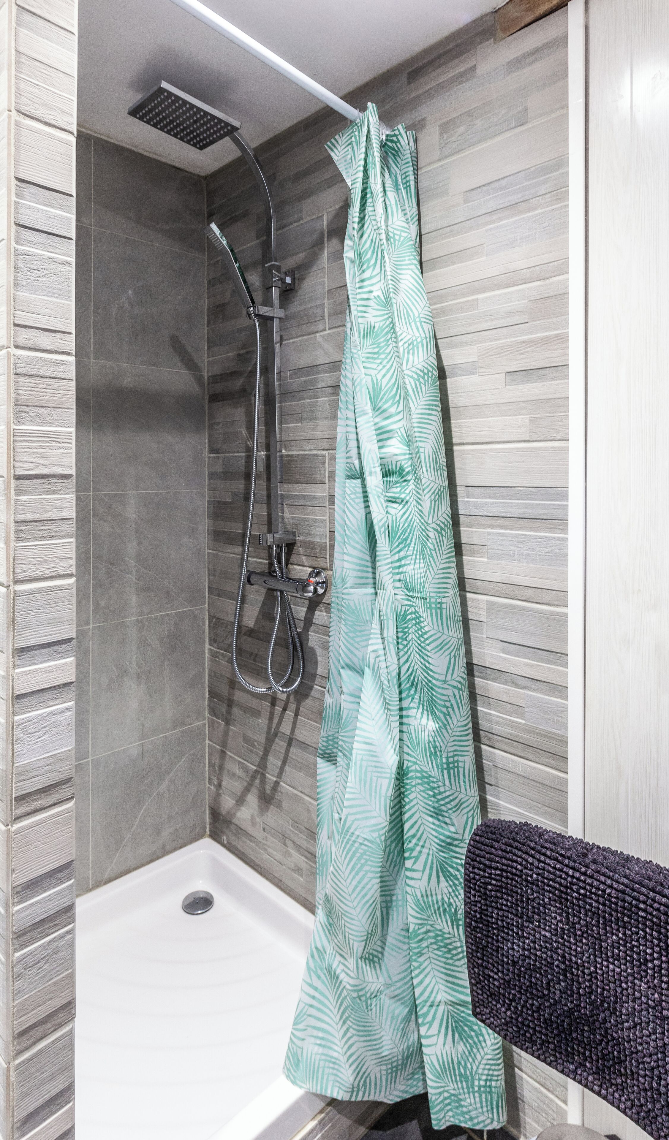 A shower area with a glass door, a handheld showerhead, and a towel rack with a towel.