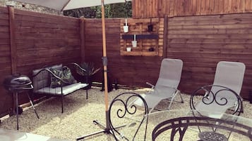 Relax in a patio with a grill, comfortable seating, and lush greenery.