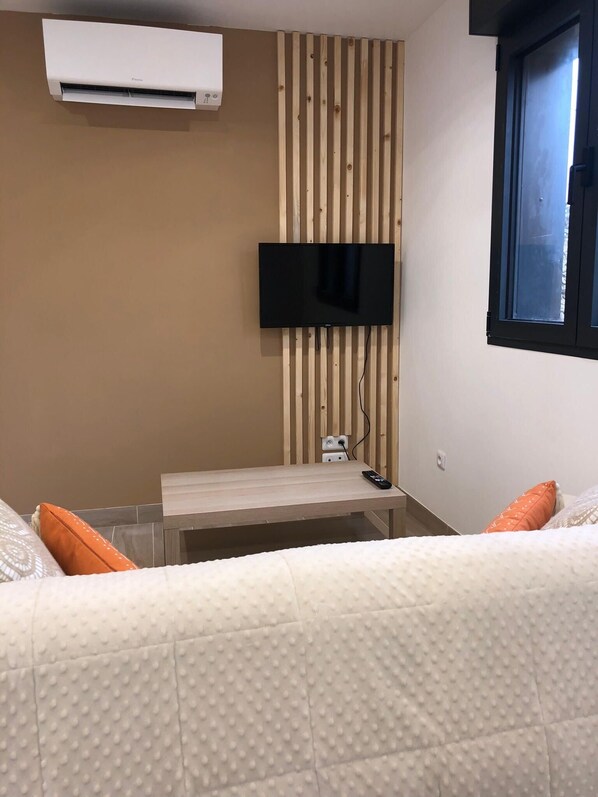 Habitación de hotel con cama, mesita de noche, televisor montado en una pared de paneles de madera y equipo de aire acondicionado.