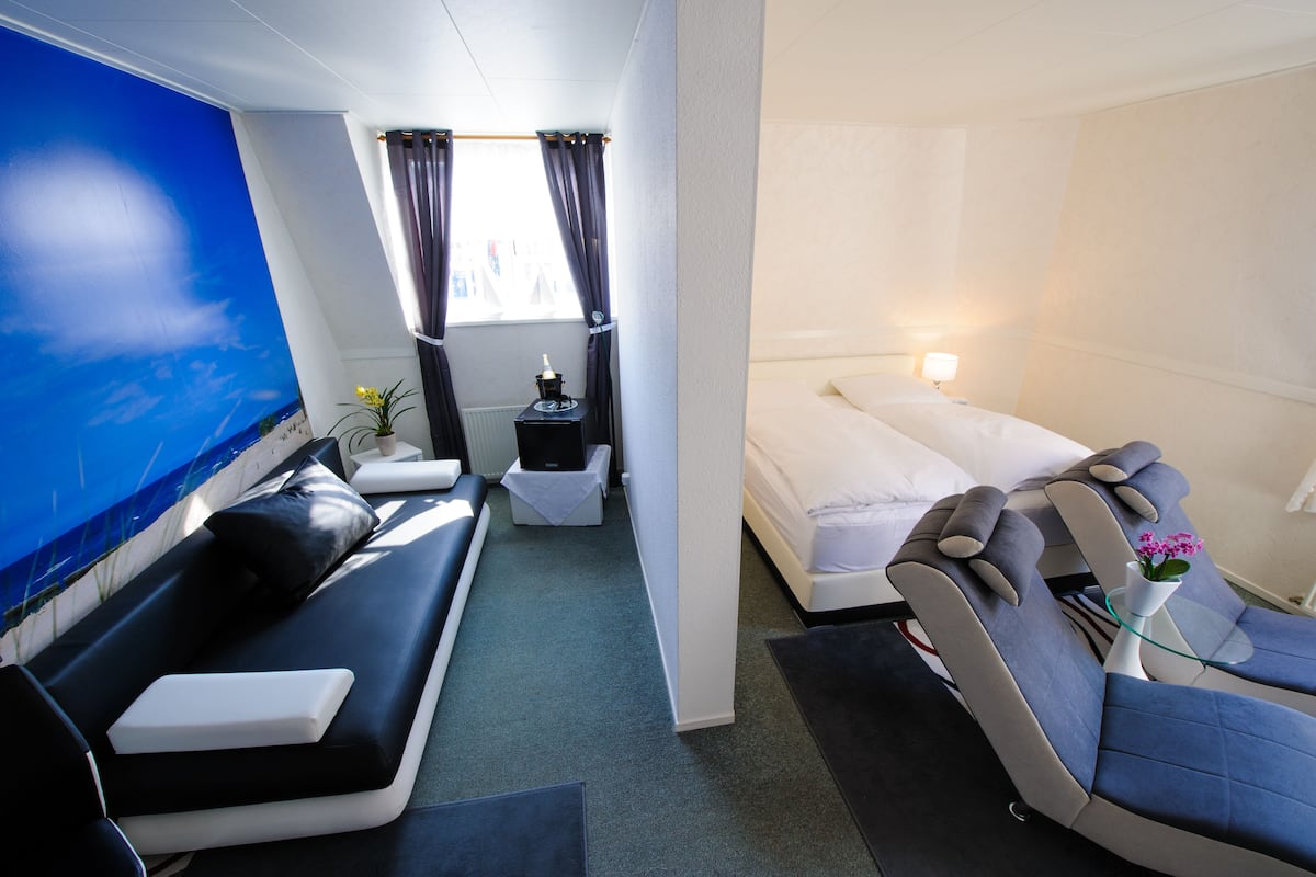 Une chambre d’hôtel moderne dotée d’une grande fenêtre, d’un canapé, d’un lit et d’un fauteuil de massage.