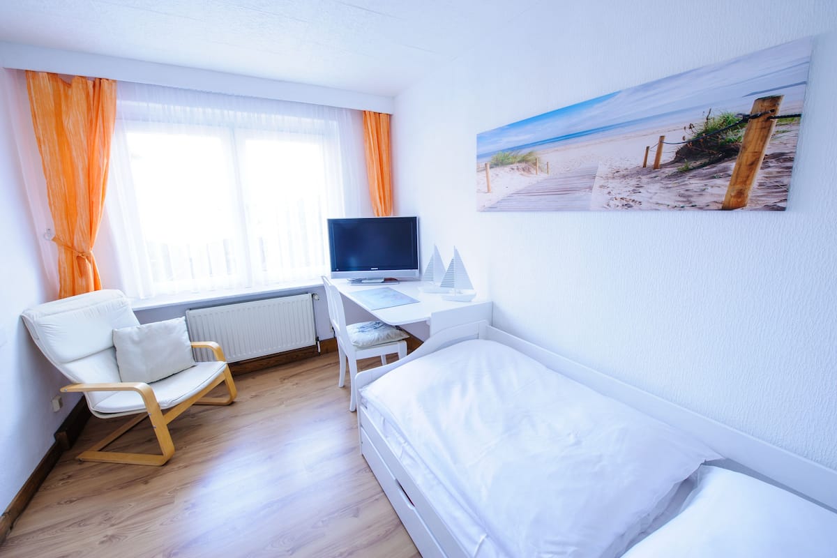 Une chambre d’hôtel avec un lit, un bureau avec un ordinateur, une chaise et une fenêtre avec des rideaux.