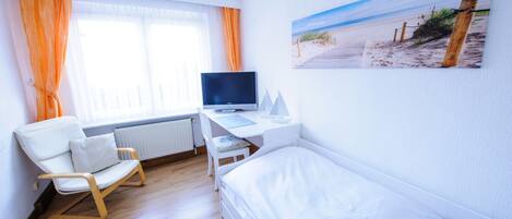 Habitación de hotel con cama, escritorio con computadora, una silla y ventana con cortinas.