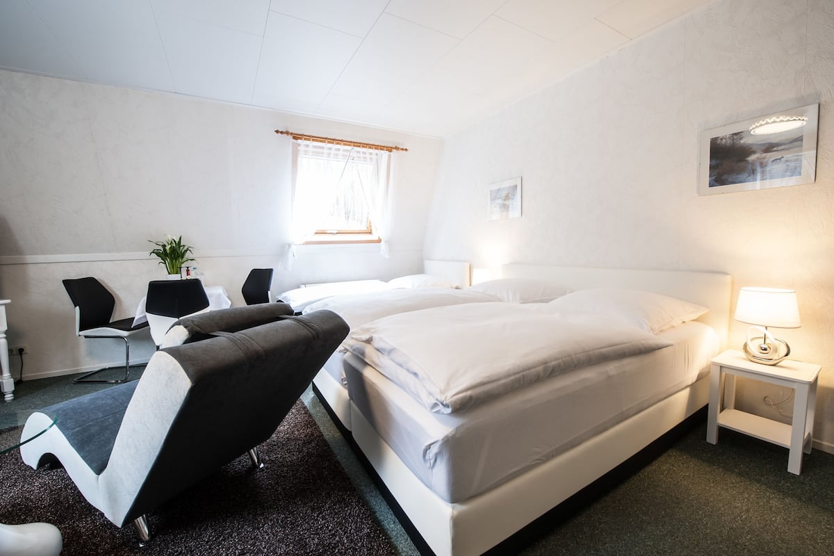 Une chambre d’hôtel avec deux lits, un bureau avec une chaise, une petite table avec une lampe et une fenêtre avec des rideaux.