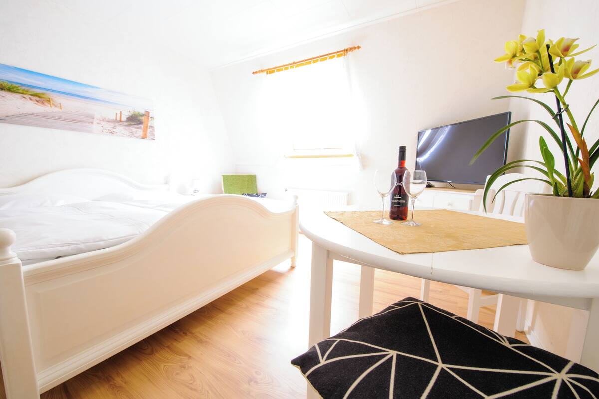 Une chambre à coucher avec un lit, une table de chevet sur laquelle se trouvent une bouteille et un verre, une télévision et une fenêtre avec des rideaux.