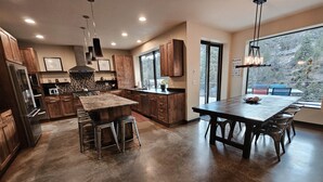 A modern kitchen with wooden cabinets, a central island, and a large dining table. - Bend River Retreat (Bend)