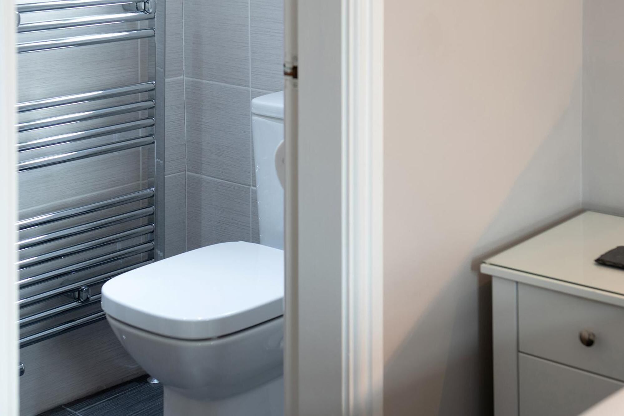 A bathroom with a white toilet, a stainless steel towel rail, and a white cabinet with a drawer.