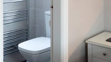 A bathroom with a white toilet, a stainless steel towel rail, and a white cabinet with a drawer.