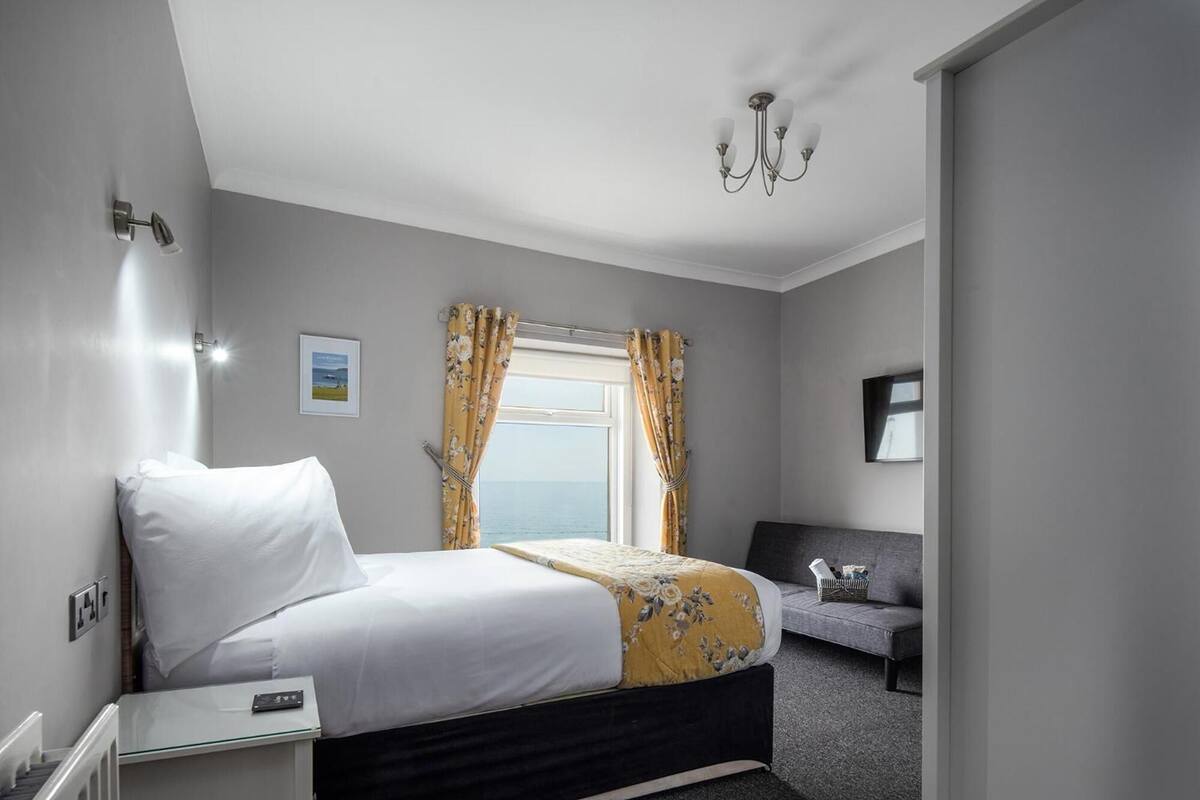 Habitación de hotel con cama, sofá, ventana con cortinas, candelabro y un cuadro en la pared.