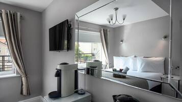 A modern hotel room with a large mirror, a bed with white linens, a coffee machine, and a kettle.