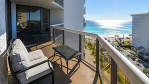 A balcony with a sofa and table, overlooking a beach and a parking area.