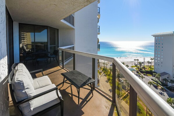 A balcony with a sofa and table, overlooking a beach and a parking area. - Contemporary cozy resort condo w/balcony & beach views! (Miramar Beach)