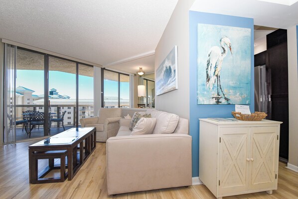 A spacious living area with a large window, a sofa, a coffee table, and a cabinet. - Contemporary cozy resort condo w/balcony & beach views! (Miramar Beach)