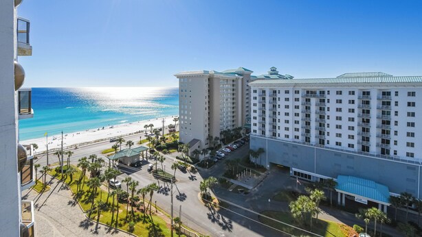 A hotel with a beachfront view, multiple floors, and a parking area with palm trees.