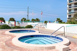 Un espace piscine comprenant deux bains à remous, une clôture blanche et un bâtiment doté de balcons.