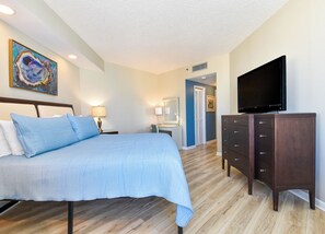 A hotel room with a bed, a dresser, a television, and a desk with a chair. - Contemporary cozy resort condo w/balcony & beach views! (Miramar Beach)