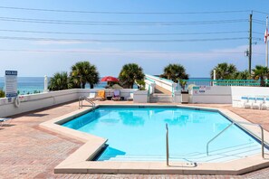 A swimming pool with a view of the ocean, surrounded by palm trees and lounge chairs.