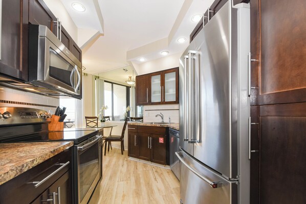 A modern kitchen with stainless steel appliances, dark wood cabinets, and a granite countertop. - Contemporary cozy resort condo w/balcony & beach views! (Miramar Beach)