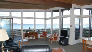 Una sala de estar con vista al mar, amoblada con un sofá, sillas, una mesa y un televisor.