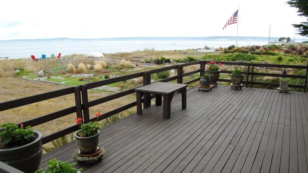 Terraza de madera con plantas en macetas y un banco con vista a la playa.