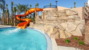 A water slide at a resort pool with a rocky backdrop and palm trees.