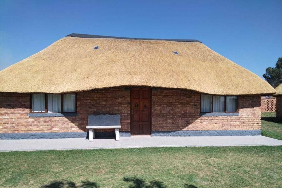 A thatched-roof building with a brick facade, a wooden door, and a bench outside.